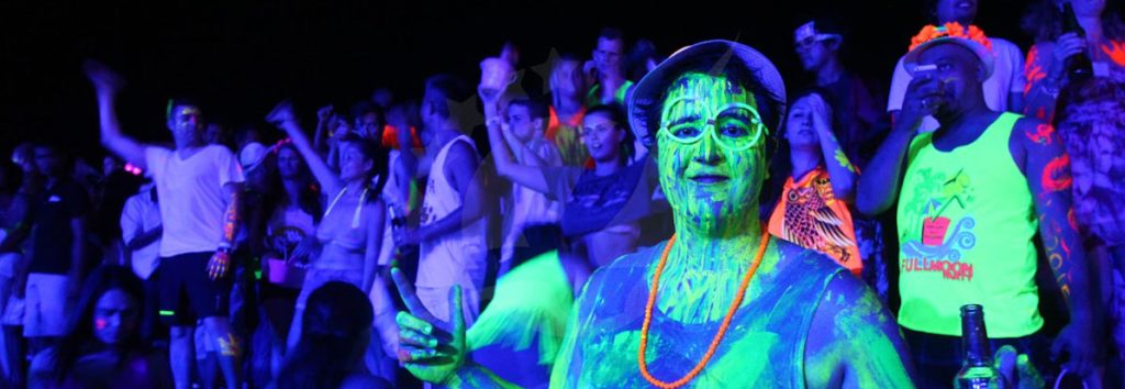 Grande multidão em evento noturno com pintura corporal néon e luz UV, pessoas a dançar e a festejar