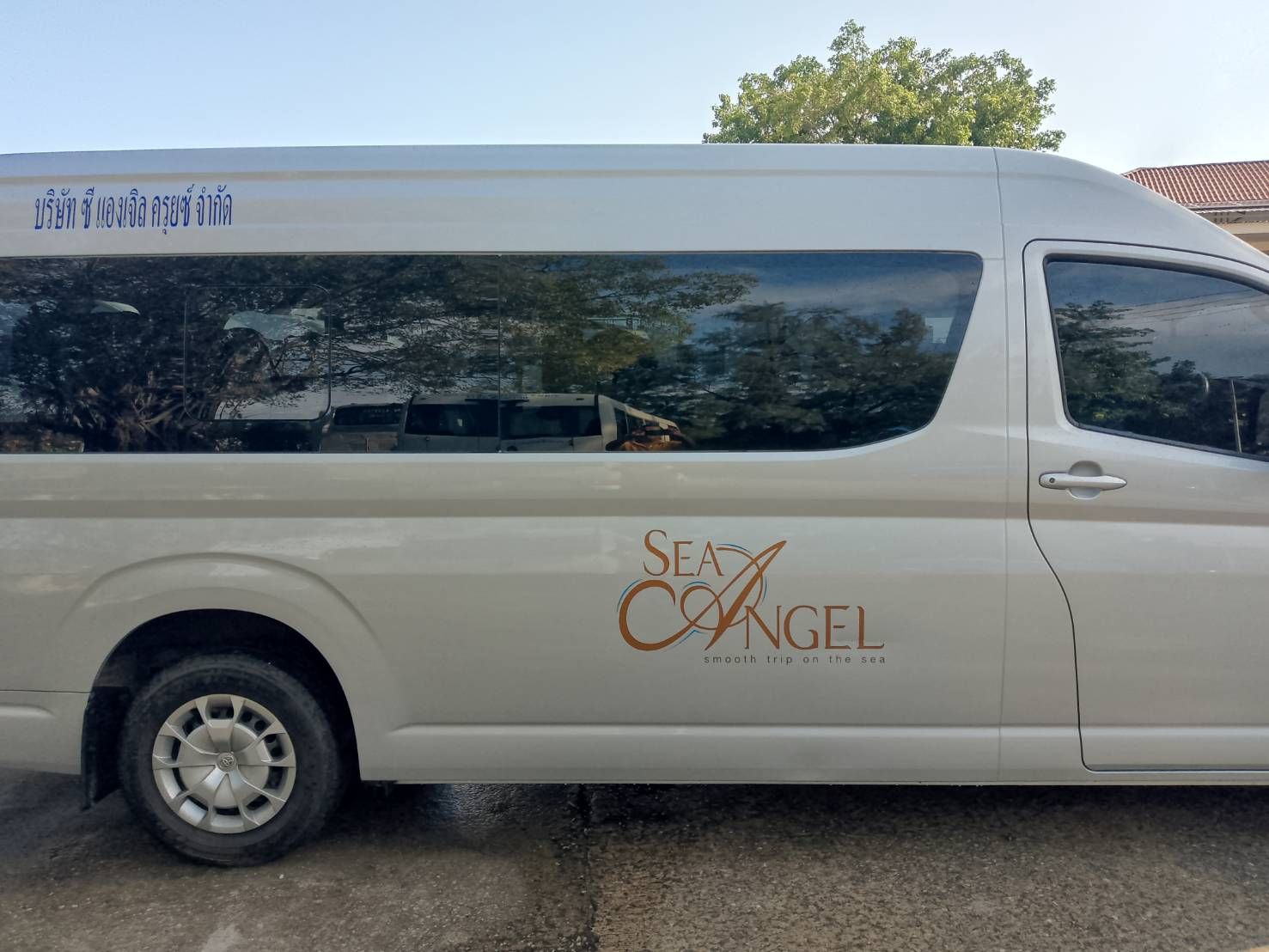 Lateral de uma carrinha de passageiros Toyota branca com o logótipo da transportadora "Sea Angel" e letras tailandesas, estacionada no exterior