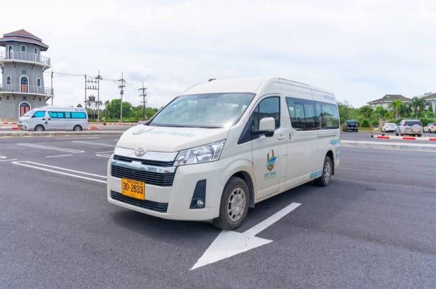 Furgoneta turística Toyota Hiace branca com matrícula tailandesa estacionada num parque de asfalto vazio sob céu nublado