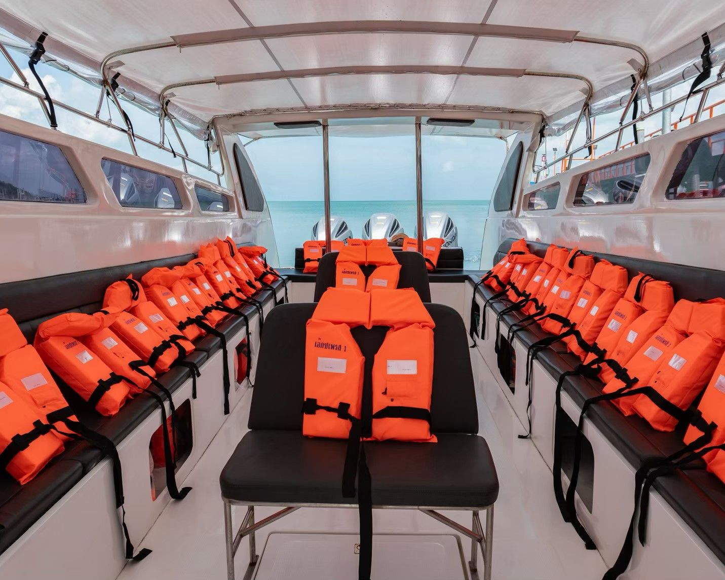 Cabina vazia de lancha com coletes salva-vidas laranja nos bancos pretos, mar e motores fora de borda à popa