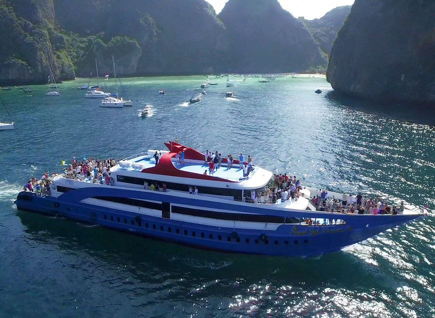 Barco de passageiros azul e branco cheio de gente numa baía turquesa rodeada de falésias calcárias, Tailândia