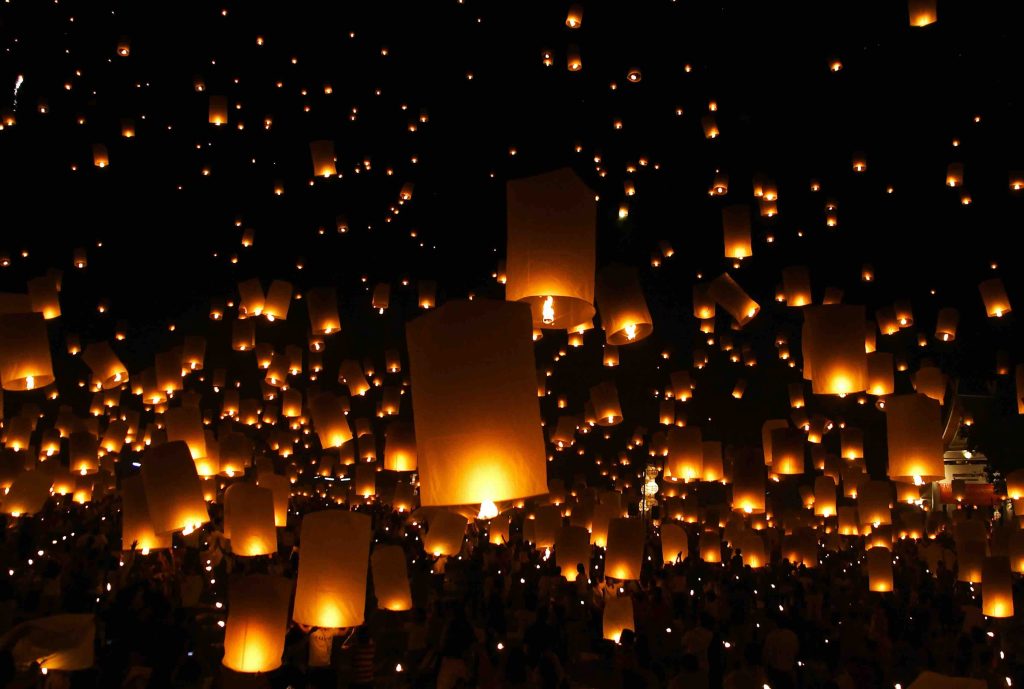 Centenas de lanternas de papel iluminadas a subir no céu noturno sobre uma multidão em silhueta