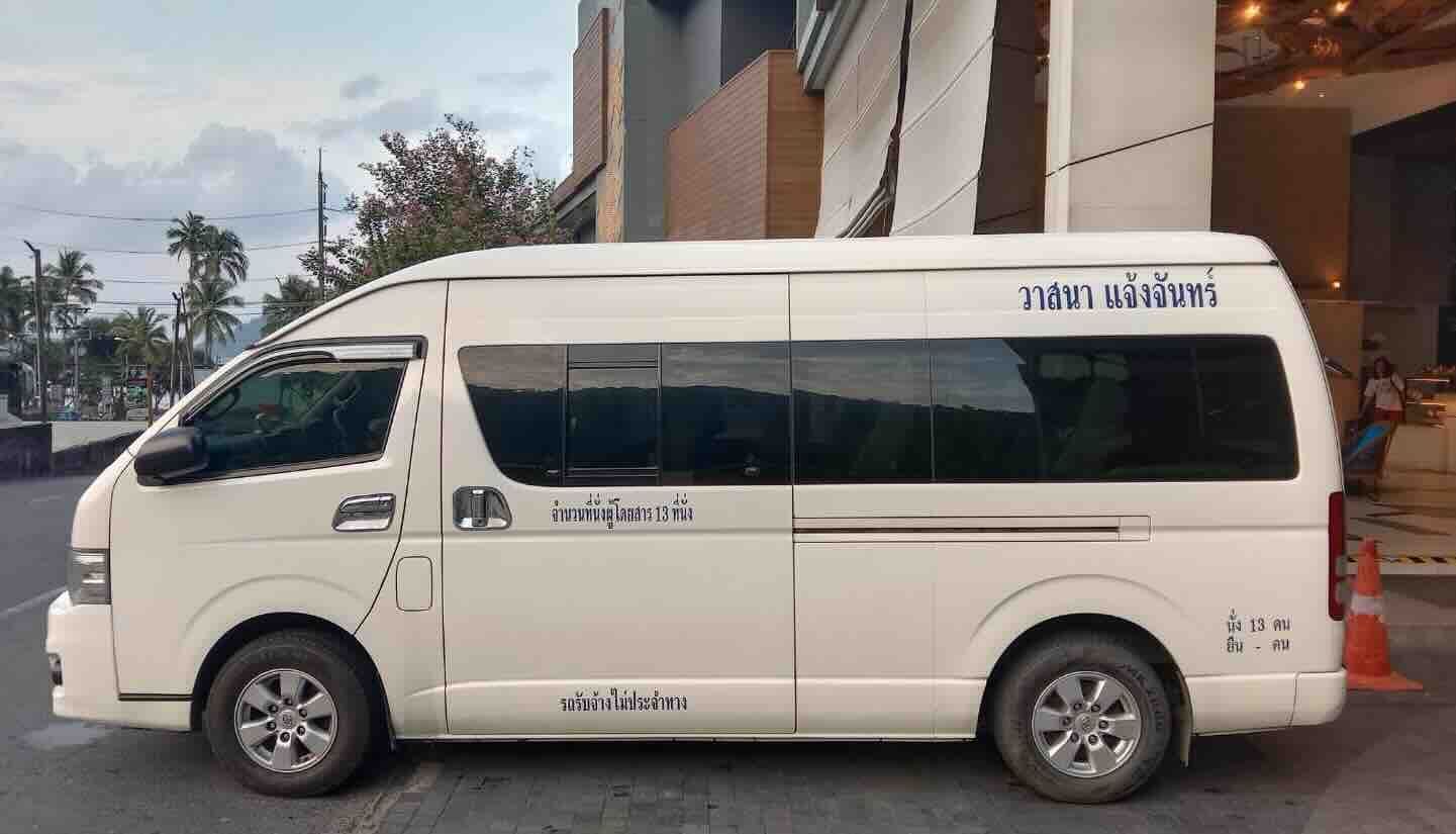 Furgoneta Toyota Hiace branca de 13 lugares estacionada de lado à entrada de um hotel na Tailândia, com texto tailandês na carroçaria