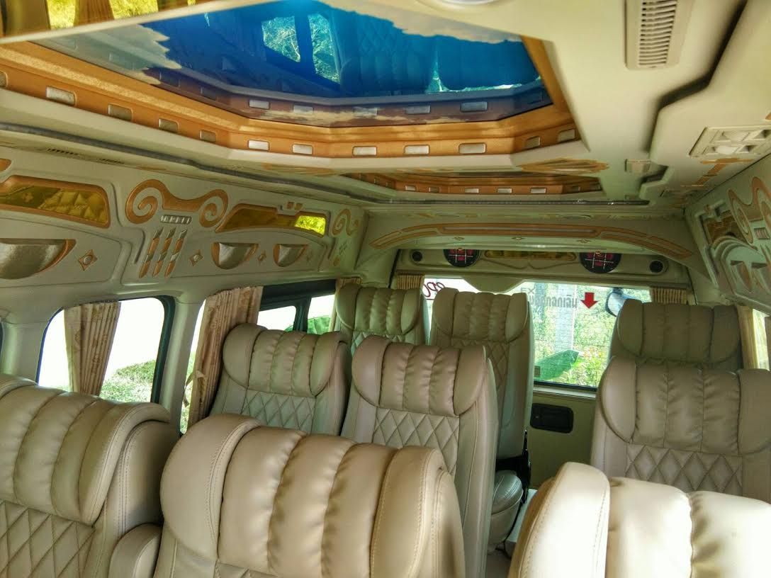 Interior de uma minivan com assentos de couro bege matelassado, painéis de teto decorativos e clarabóia com tonalidade azul