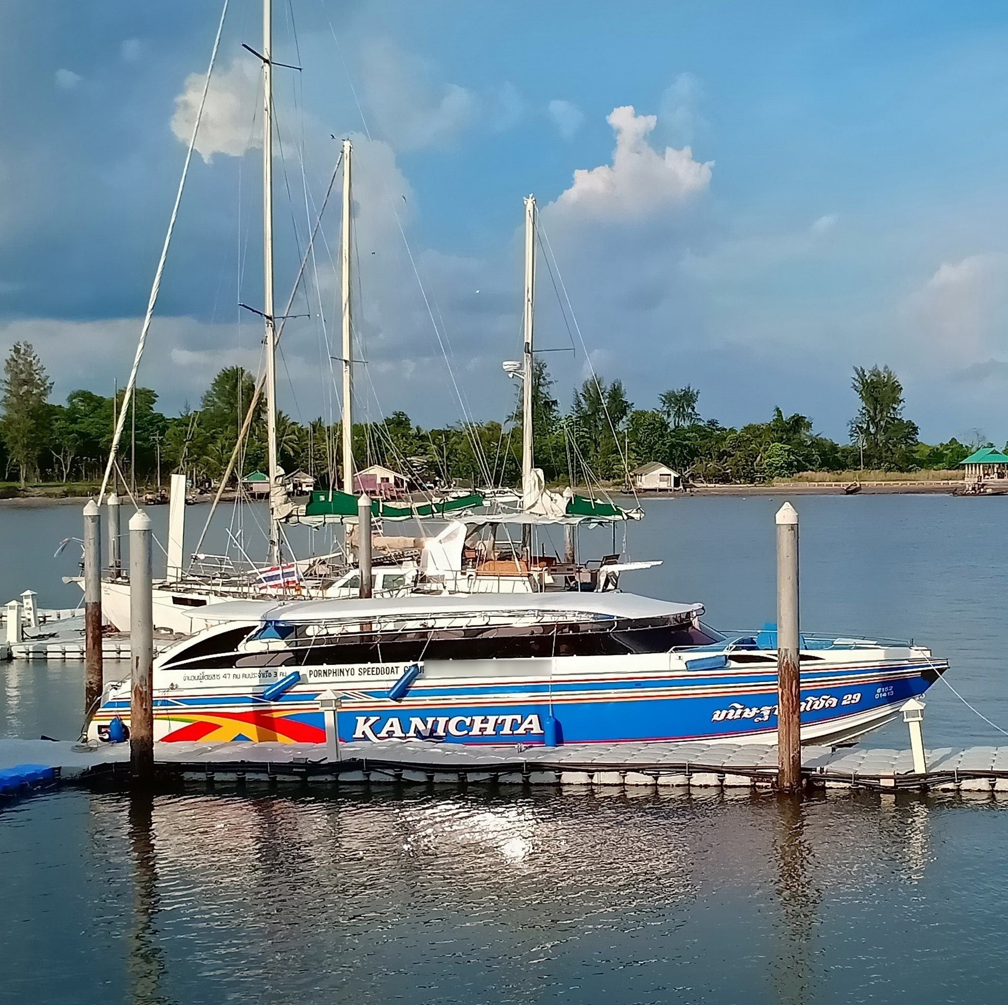 Ferry-lancha azul e branco "Kanichta" atracado num pontão flutuante junto a veleiros na Tailândia