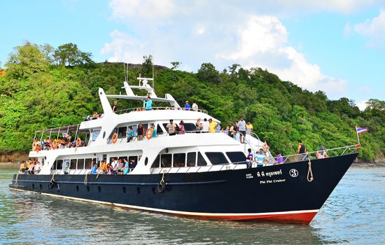 Barco de passageiros Phi Phi Cruiser com turistas no deck a navegar junto a uma ilha arborizada sob céu azul
