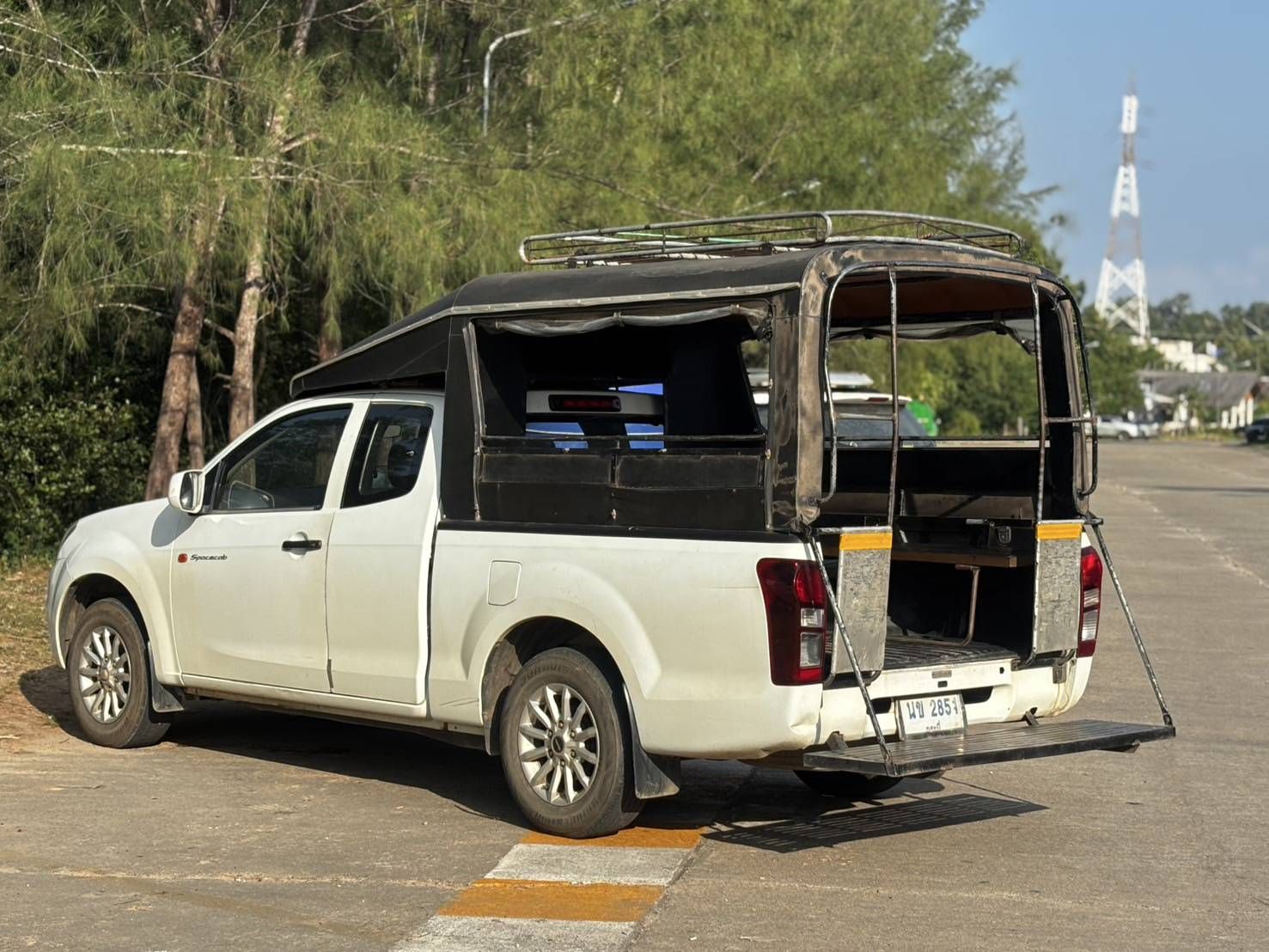 Pick-up branca convertida em songthaew, táxi partilhado com bancos corridos e porta-bagagens no teto, estacionada na estrada