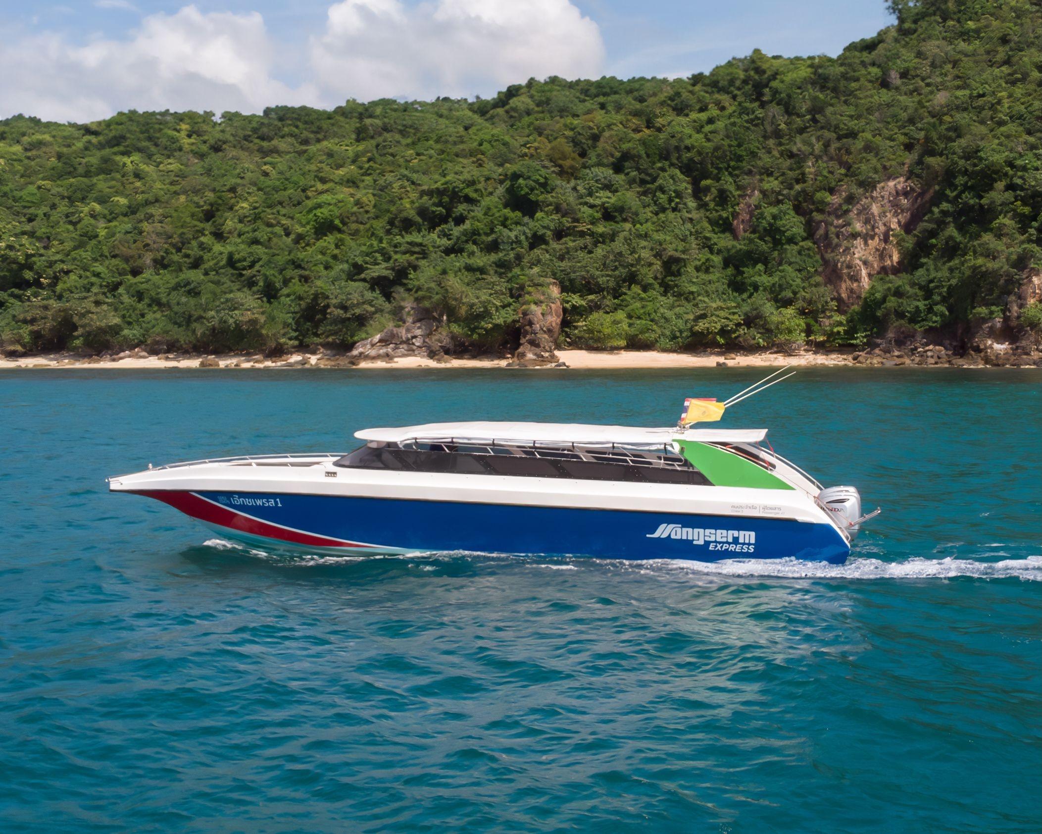 Lancha Songserm Express azul e branca a navegar em água turquesa junto à costa rochosa arborizada de uma ilha
