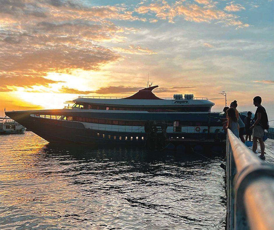 Grande ferry de passageiros atracado num cais ao pôr do sol enquanto viajantes esperam junto à amurada