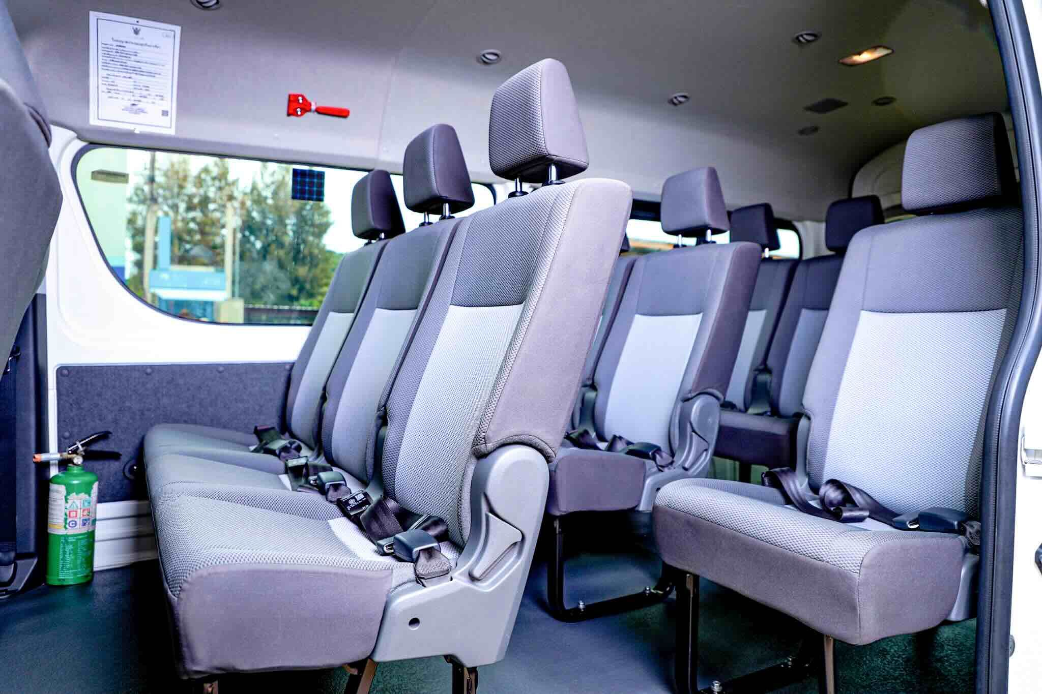 Interior of an empty minivan shuttle with grey fabric passenger seats, seat belts and a fire extinguisher