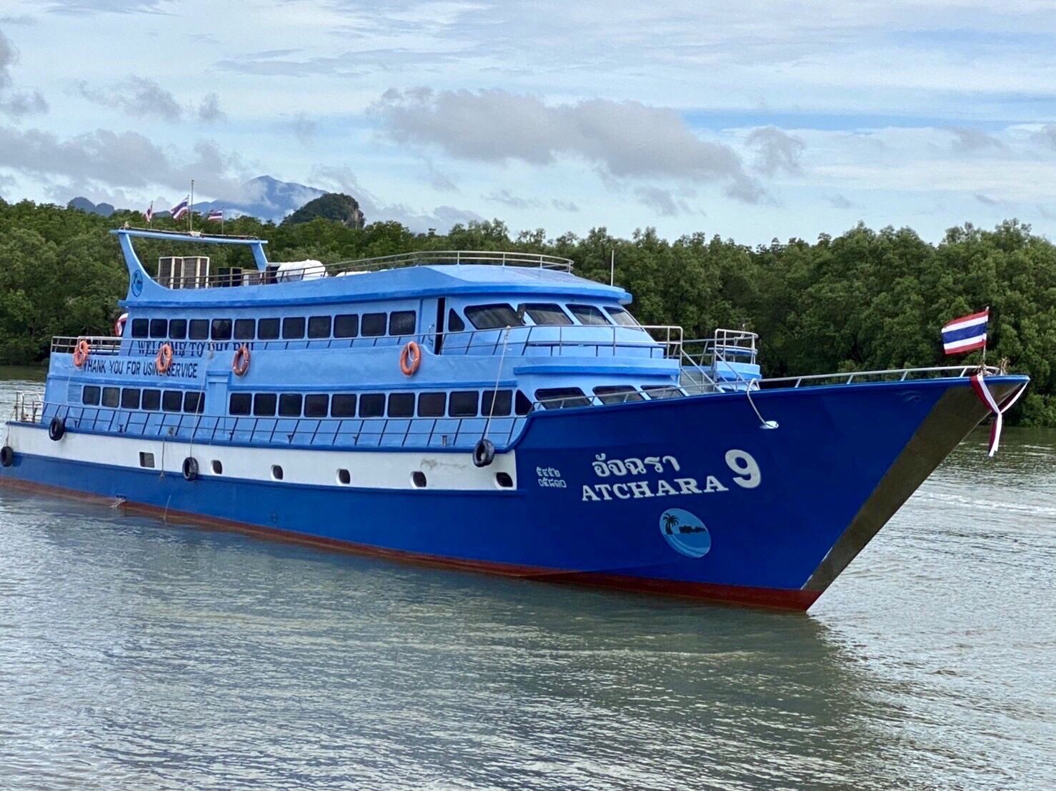 เรือโดยสารไทยสีฟ้า-ขาว "อัจฉรา 9" จอดเทียบในน้ำนิ่งข้างชายฝั่งป่าโกงกาง