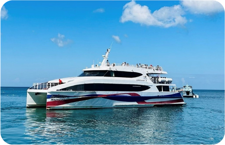 Ferry catamarã rápido branco com faixas vermelhas e azuis no casco, fundeado em mar turquesa calmo sob céu azul