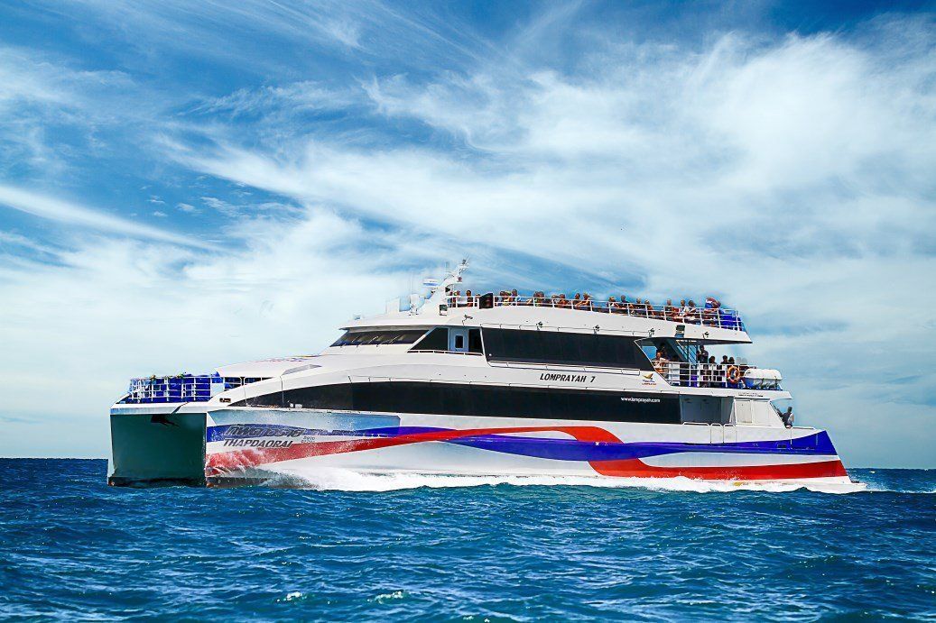 Ferry catamarã rápido da Lomprayah com casco vermelho, branco e azul a navegar em mar azul aberto sob nuvens cirros