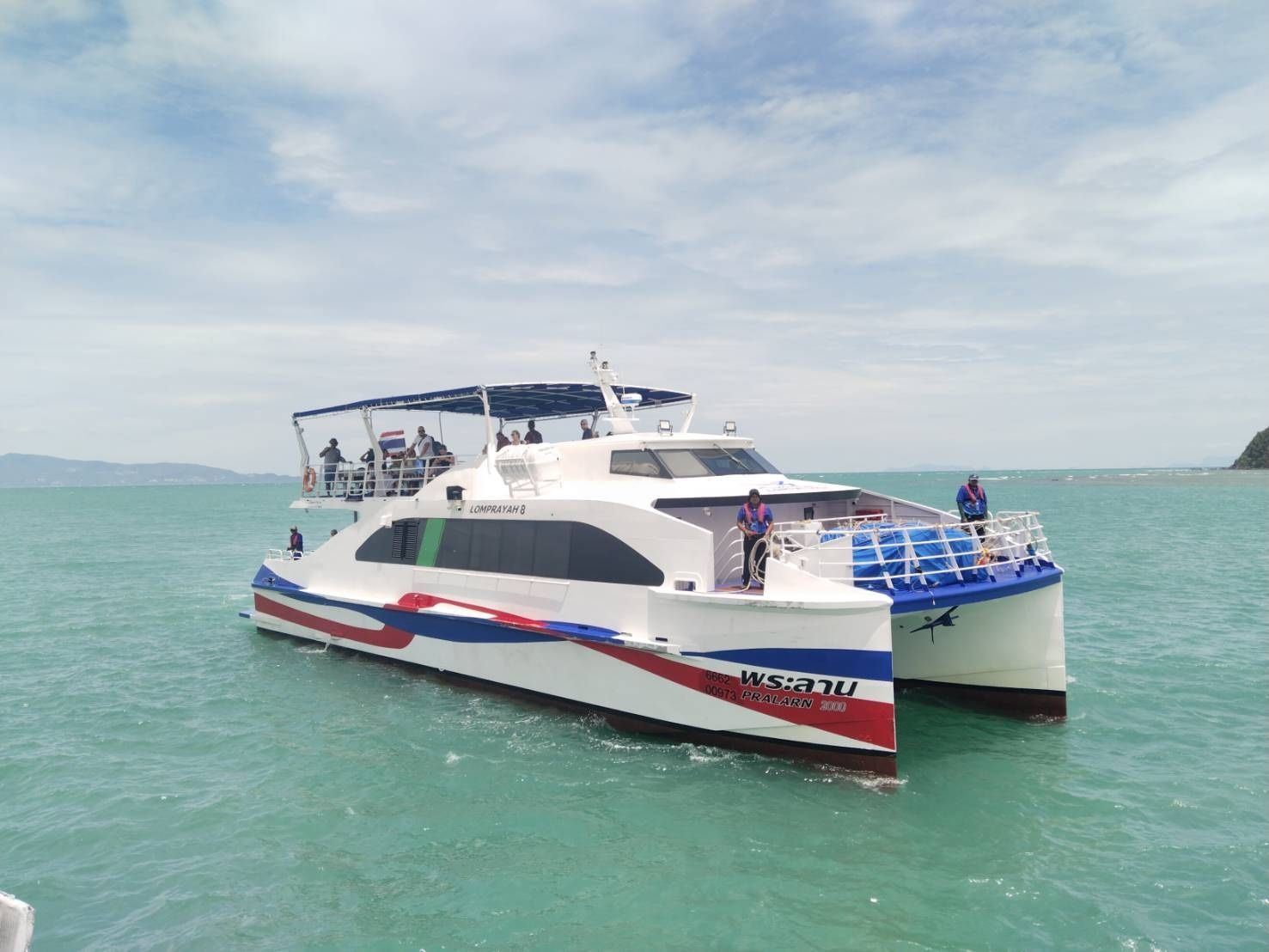 Ferry catamarã rápido da Lomprayah com pintura vermelha, branca e azul fundeado em mar turquesa junto a um promontório
