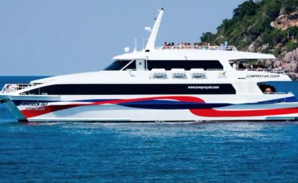 White high-speed catamaran ferry with red and blue livery cruising past a rocky green island in calm turquoise sea
