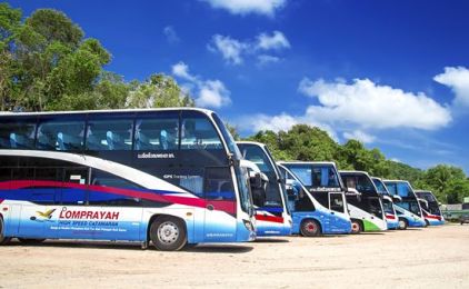 Fila de autocarros Lomprayah estacionados na diagonal num parque de gravilha sob céu azul brilhante com nuvens