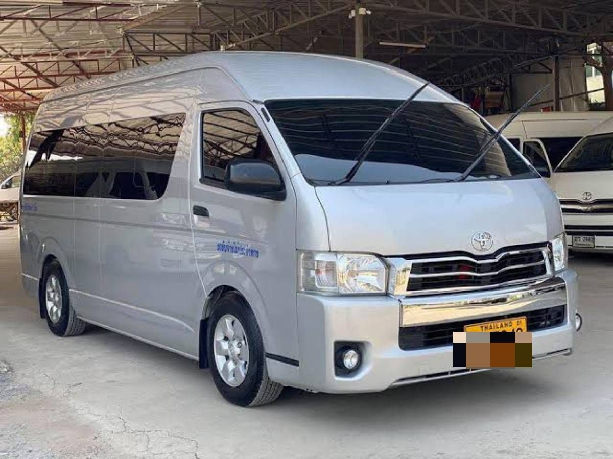 Minibus Toyota Hiace prateado de tejadilho alto num depósito aberto com outras carrinhas, matrícula tailandesa
