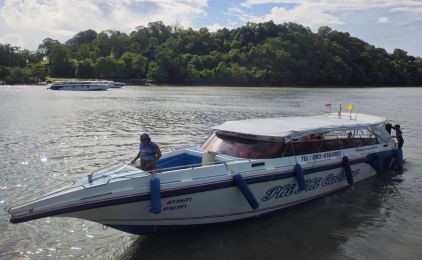 Lancha branca e azul ancorada em água calma junto a um promontório arborizado, com uma segunda lancha ao largo