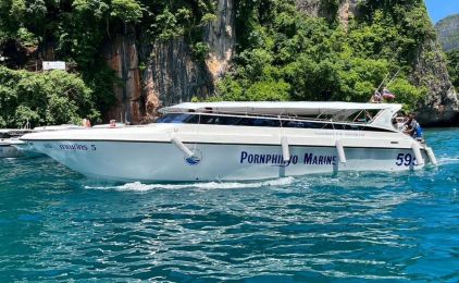 Lancha rápida branca com a inscrição «Pornphinyo Marine 599» atracada em água turquesa sob falésias calcárias na Tailândia