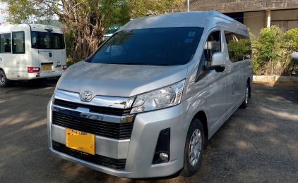 รถตู้โดยสาร Toyota Hiace สีเงินป้ายทะเบียนรถรับจ้างสีเหลือง จอดข้างรถมินิบัสสีขาว