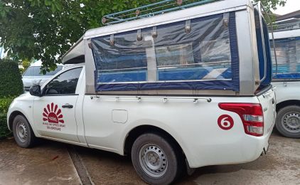 Camioneta branca com cobertura para passageiros e o número 6 a vermelho estacionada num parque pavimentado junto a vegetação