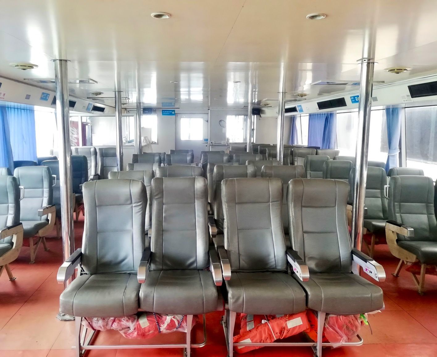Bancos de pele cinzentos vazios na cabina de um ferry com coletes salva-vidas laranja por baixo e chão vermelho