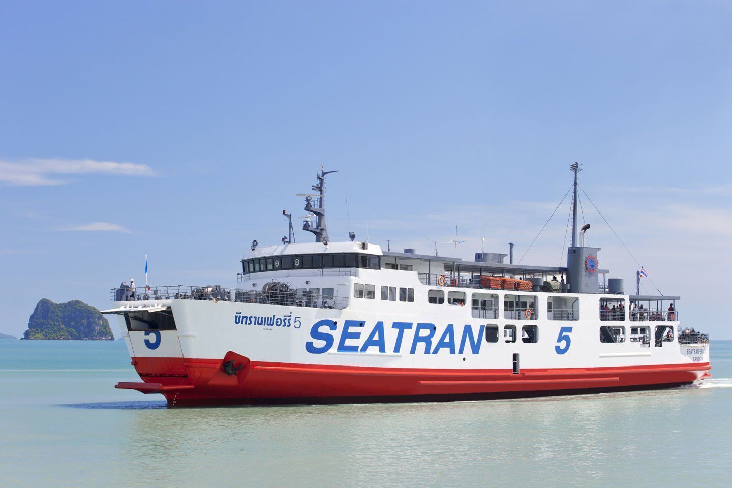 Ferry de passageiros Seatran vermelho e branco a navegar em mar turquesa calmo com uma pequena ilha calcária ao fundo