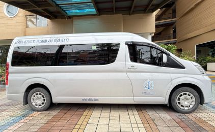 Silver minivan parked outside a hotel entrance, Thai lettering across the side windows and an anchor logo on the door