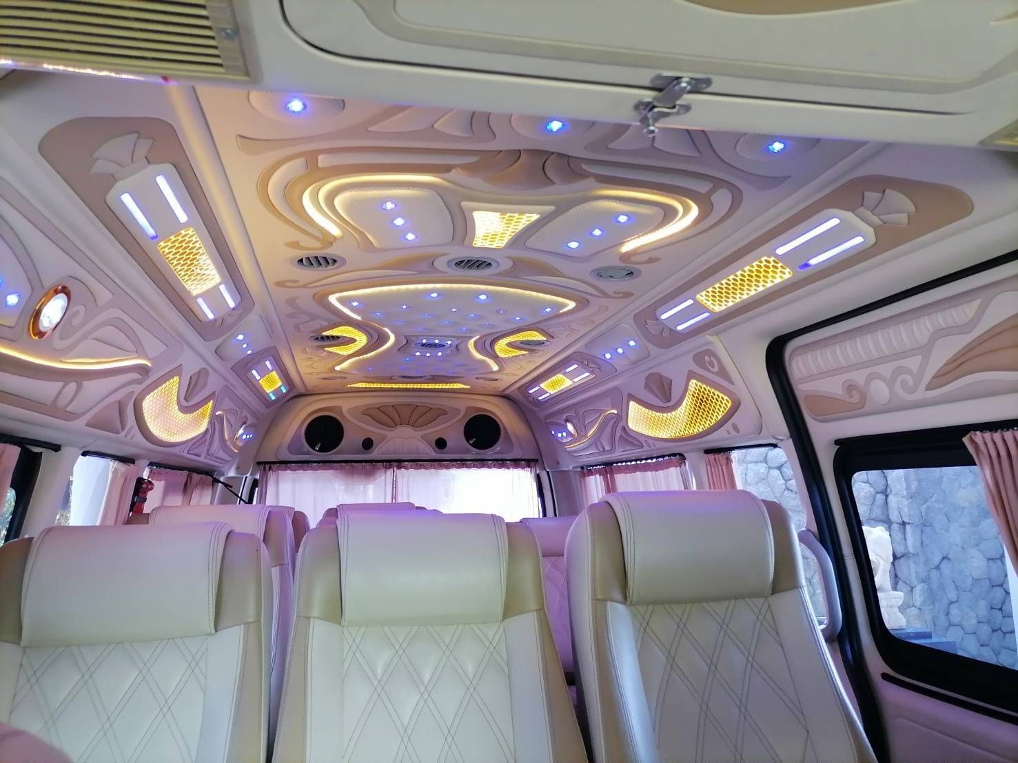 Interior de carrinha VIP com teto esculpido, luzes LED, bancos de pele creme e cortinas cor-de-rosa