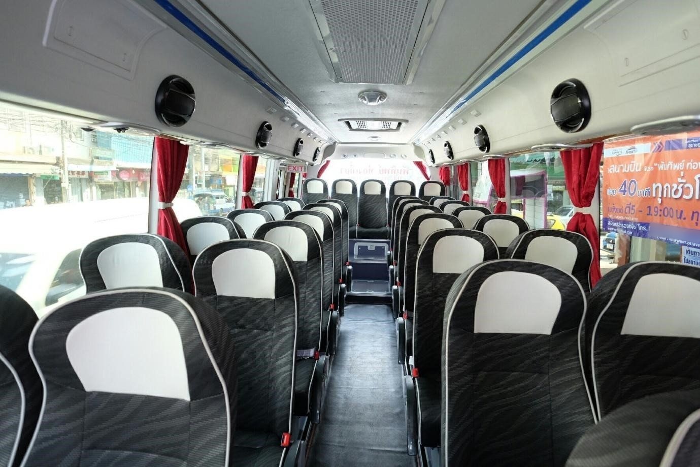 Leerer Innenraum eines thailändischen Reisebusses mit schwarz-weißen Sitzen, roten Vorhängen und Lautsprechern