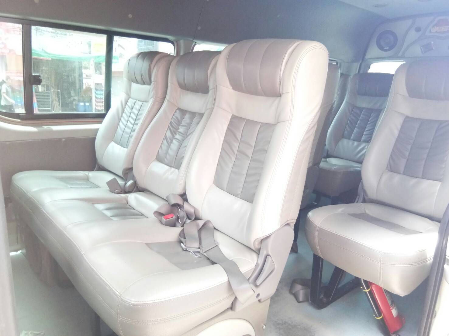 Innenraum eines Minivans mit creme-grauen Leder-Liegesitzen, Gurten und Gang, durch Seitenfenster gesehen