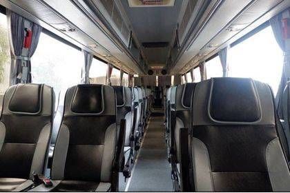 Empty interior of a coach bus with rows of dark reclining seats, aisle and overhead luggage racks