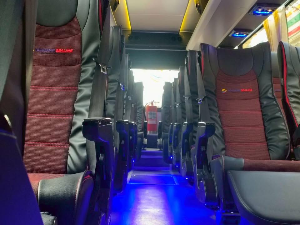 Empty coach bus interior with red and black reclining seats, blue LED aisle lighting and a fire extinguisher mid-aisle