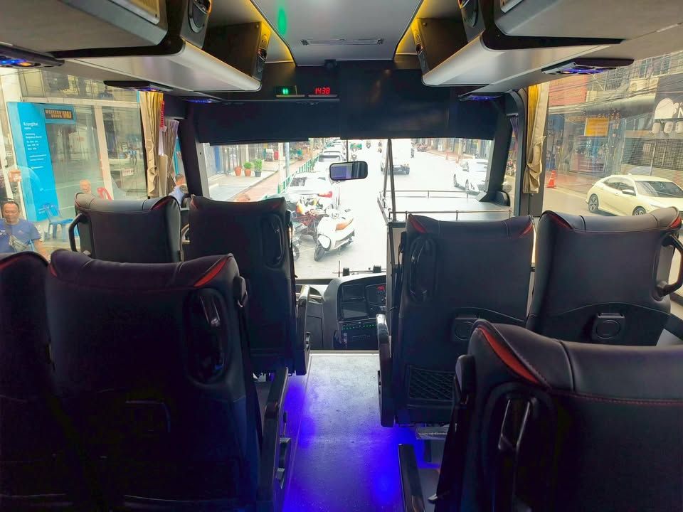 Interior of a minibus looking forward past black leather seats to a Thai street through the windscreen