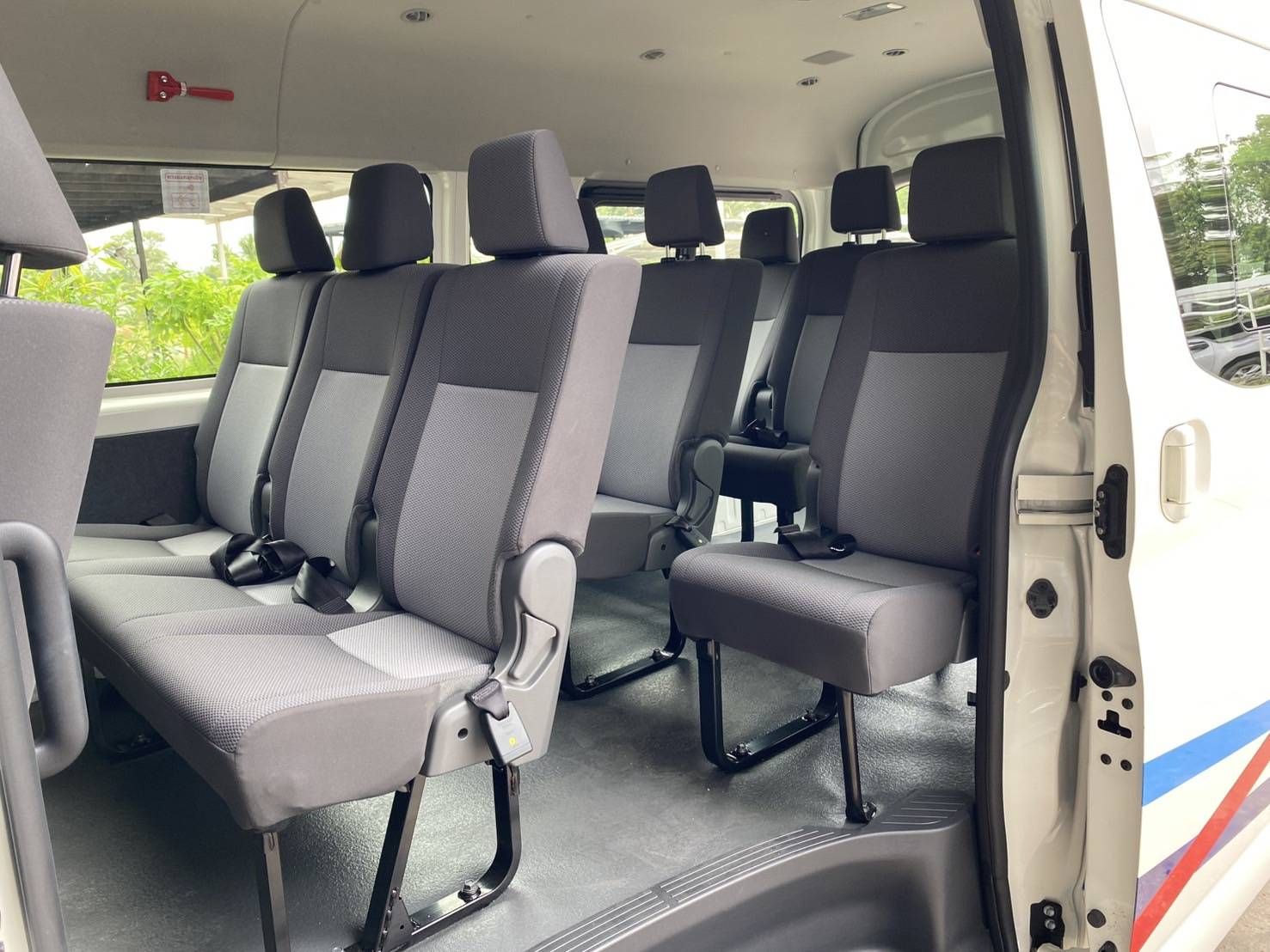Bancos vazios de tecido cinzento no interior de uma minivan branca de passageiros, vistos pela porta lateral aberta