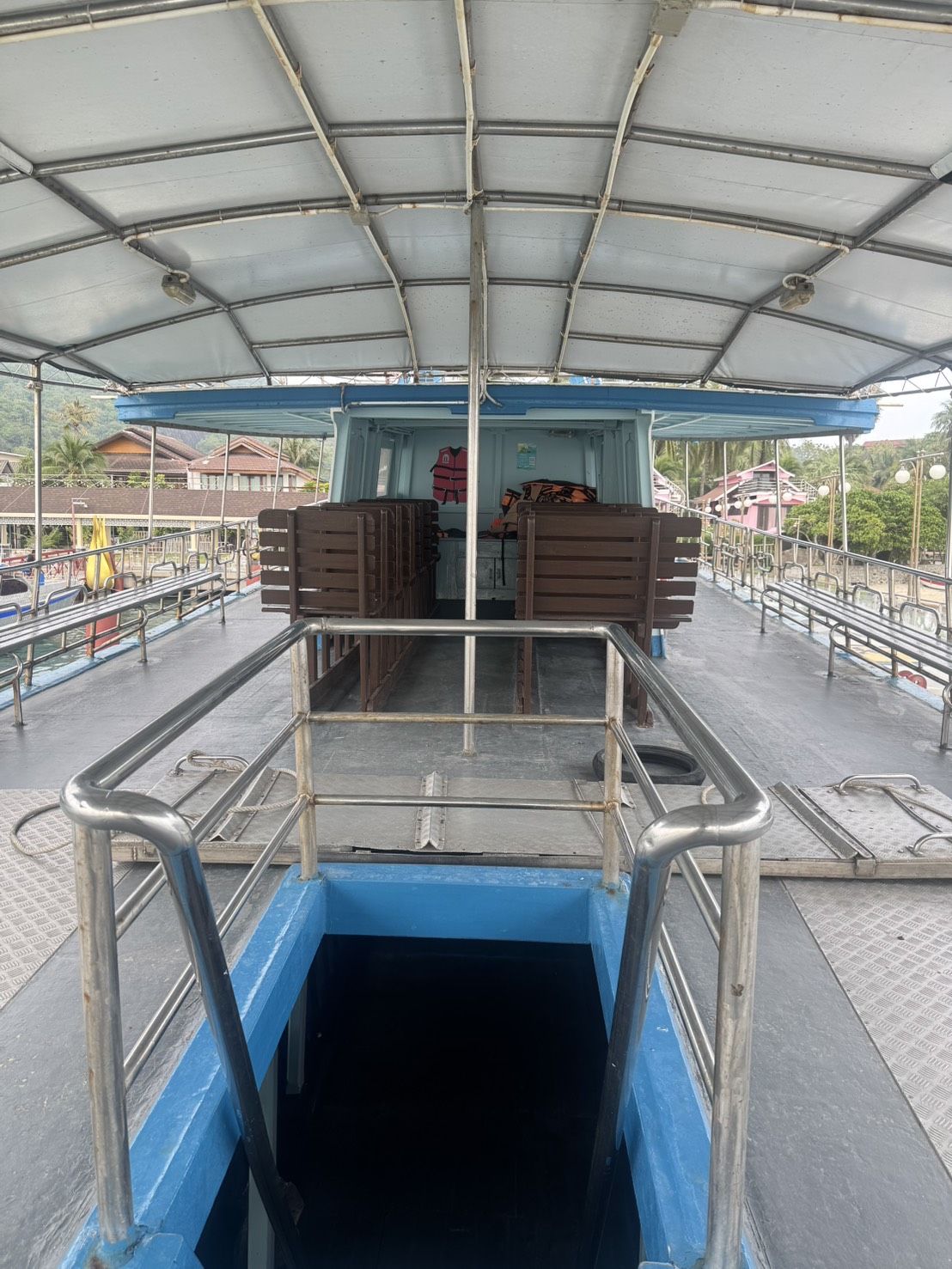 Deque superior vazio de um ferry de passageiros com toldo branco, bancos de madeira empilhados e escada para o deque inferior num cais