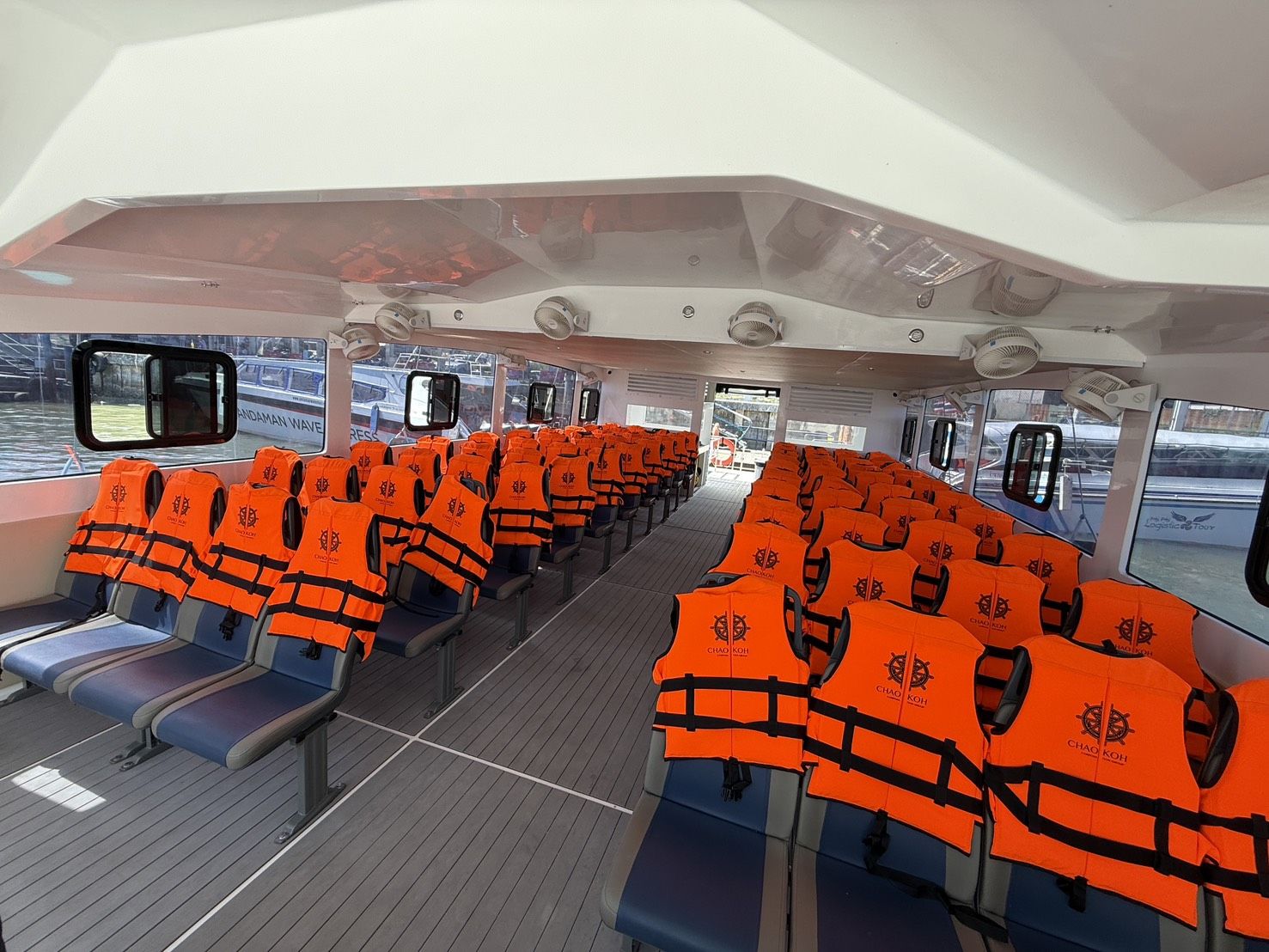 Cabina de ferry climatizada vazia com filas de bancos azuis cobertos por coletes salva-vidas laranja e janelas amplas