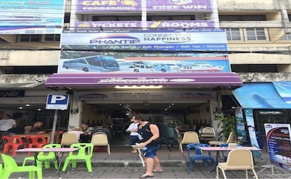 Vista de rua de um colorido café à beira-mar com cadeiras de plástico e letreiros, no Sudeste Asiático