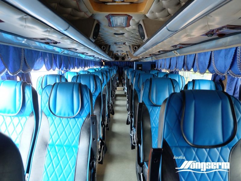 Vista do corredor no interior de um autocarro de longo curso com filas de assentos reclináveis de couro azul acolchoado e cortinas azuis
