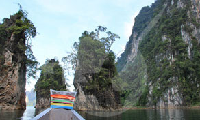 Proa de um barco longtail com faixas pintadas coloridas a atravessar um lago verde entre falésias calcárias