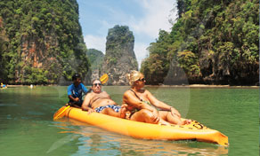 Três turistas a remar num caiaque de mar amarelo junto a falésias calcárias na baía de Phang Nga, Tailândia