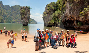 Grupo de turistas posa na praia da Ilha de James Bond, baía de Phang Nga, com rochas calcárias atrás