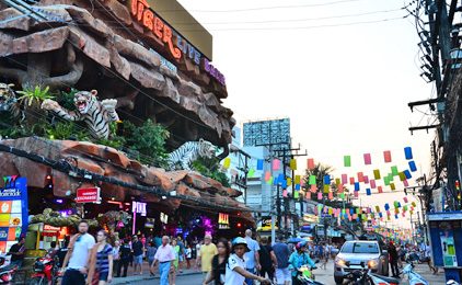 Turistas e trânsito na Bangla Road, Patong, junto a um complexo de vida noturna com fachada rochosa, estátuas de tigres e bandeiras coloridas